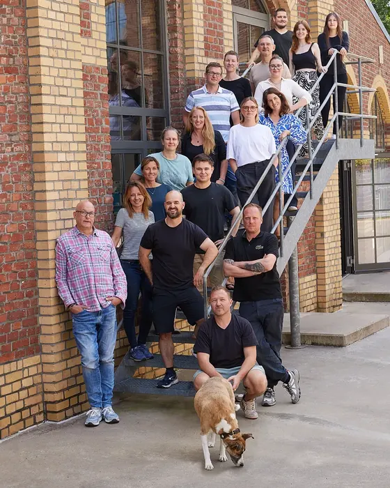 Das Team von alle freiheit auf einer Außentreppe am Büro in Köln-Ehrenfeld, vorne der Bürohund